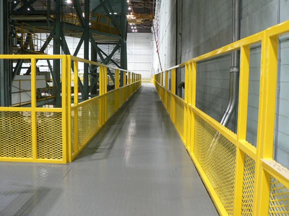 Elevated catwalk with yellow safety railings between industrial shelving aisles