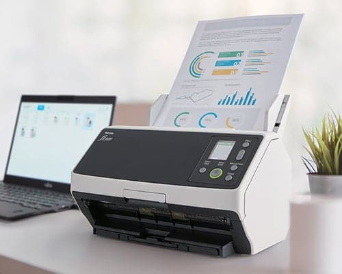 Desktop document scanner beside a laptop with a report loaded in its feeder.